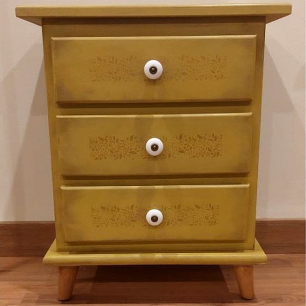 Vista frontal de una mesilla amarilla de tres cajones, pintada en amarillo y envejecida con ceras