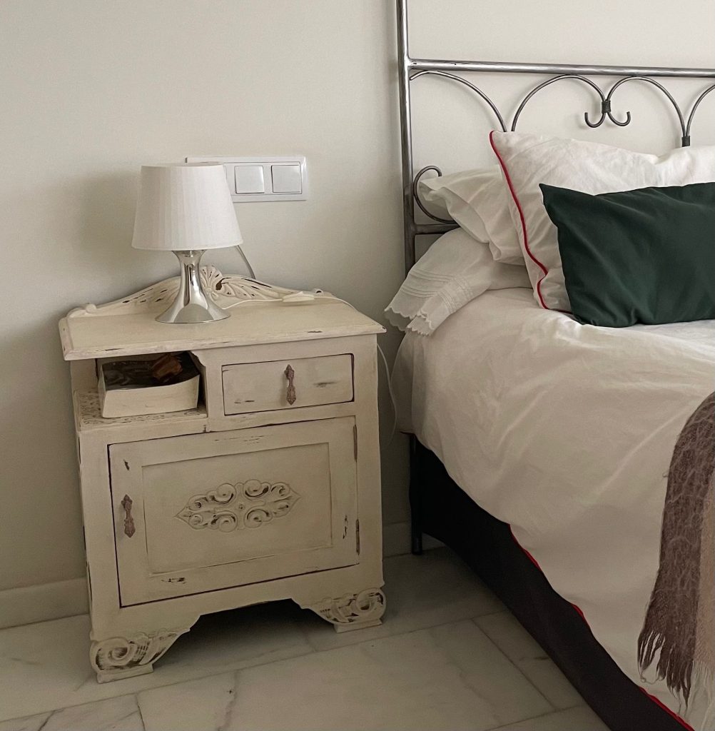 Vista frontal de mesita de noche antigua pintada de blanco antiguo.